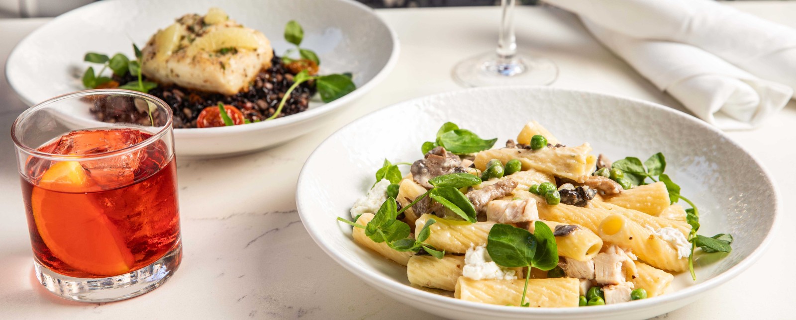 Plated pasta and fish dishes at Wolfgang Puck Kitchen + Bar